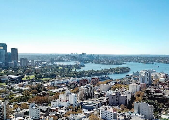 Aerial view of a coastal city with buildings, river, and bridge under a clear blue sky