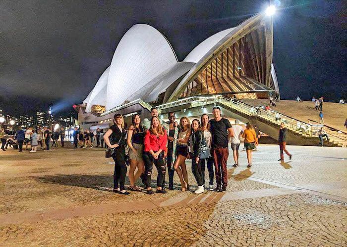 Group posing at night in front of the Sydney opera house with warm lights.
