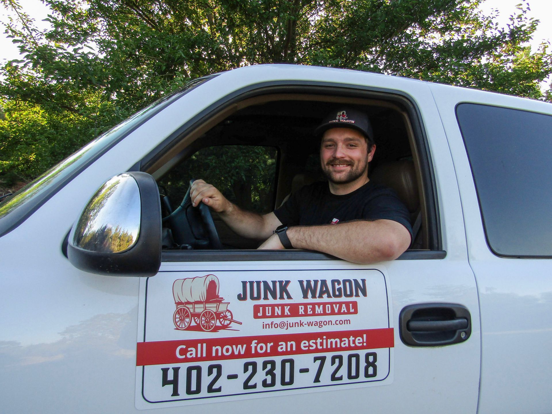 Smiling driver in white junk wagon van with “Call now for an estimate!” sign on the door