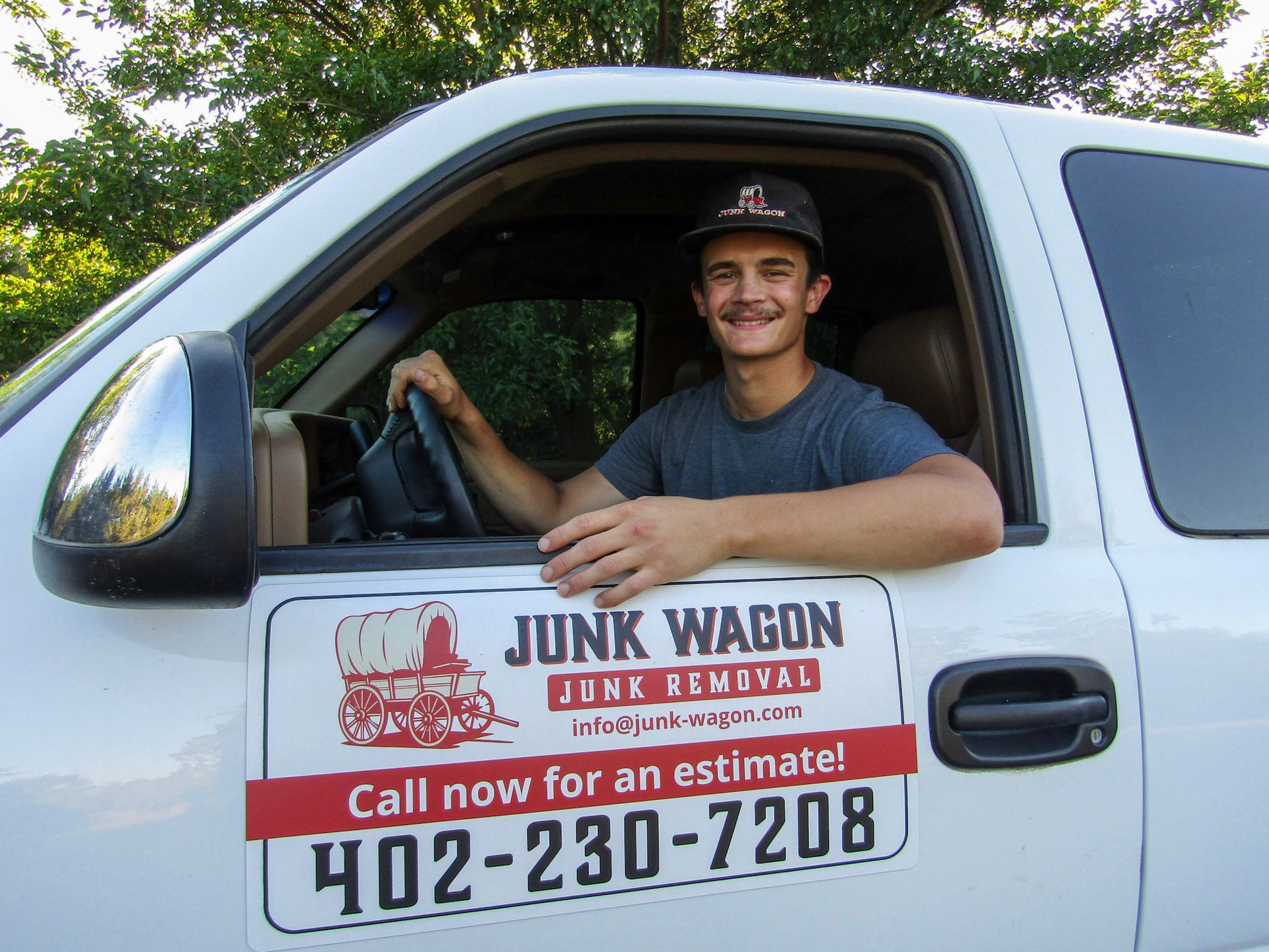 Man smiling in white truck with “Junk Wagon” sign on door and phone number 770-230-7208