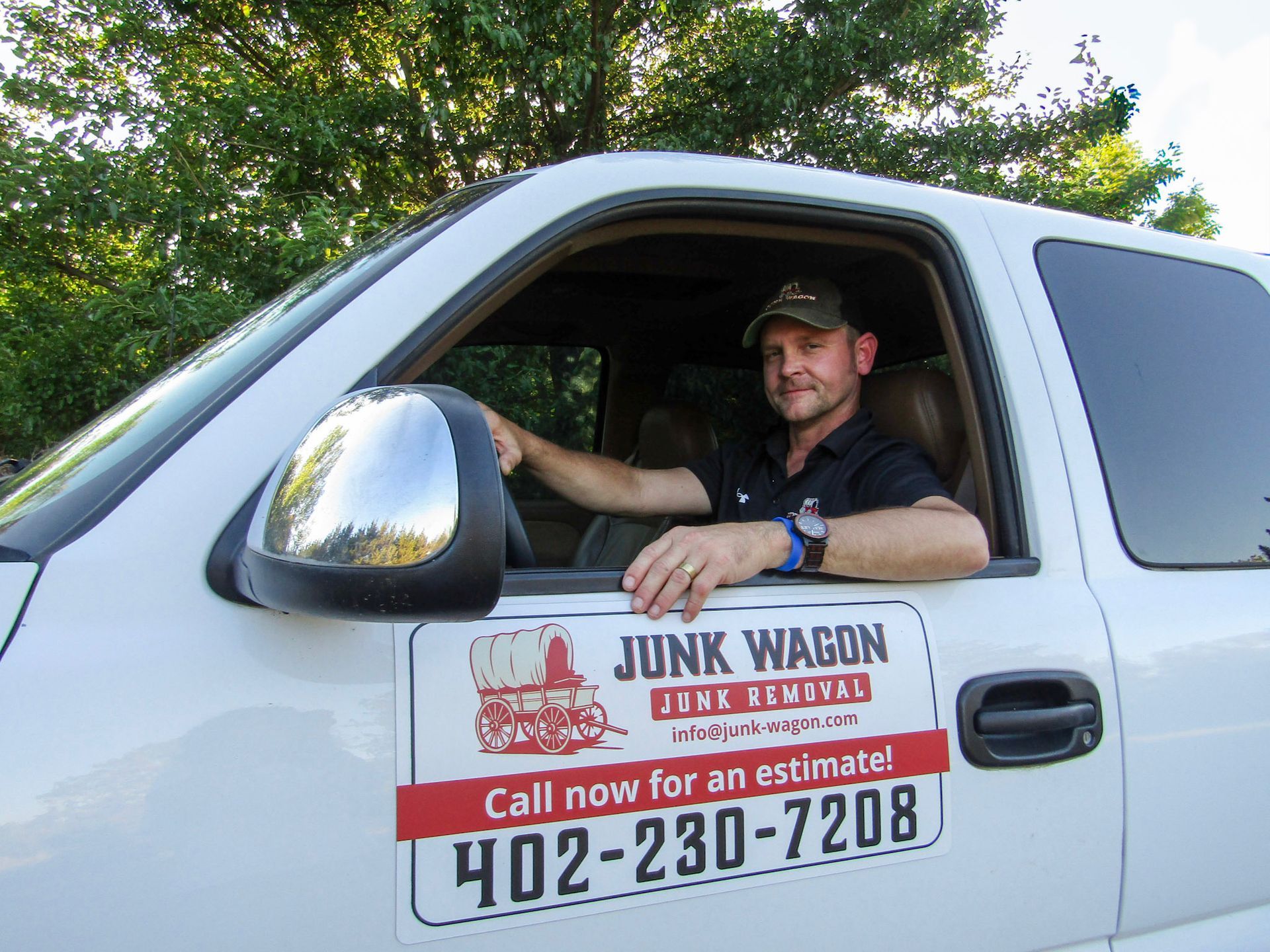 Man in a white work truck with door sign reading “Junk Wagon” and phone number 402-230-7208