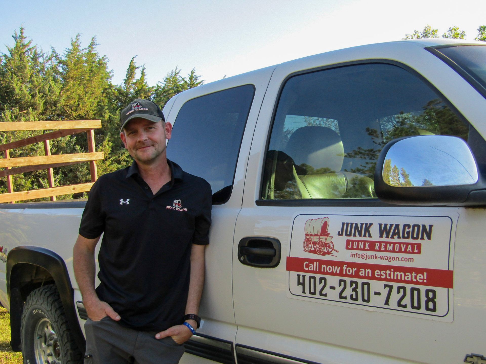 Man standing beside a white Junk Wagon truck with a company sign on the door outdoors.
