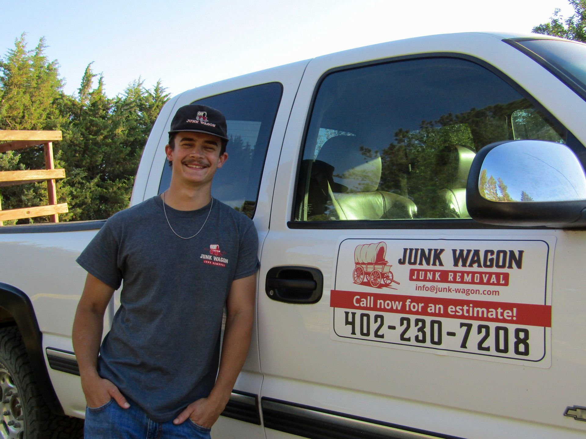 Man standing beside a white pickup truck with a “Junk Wagon” service sign on the door