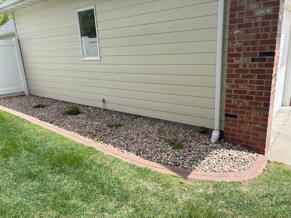 Mulched planting bed along a beige house with a small window and brick corner trim