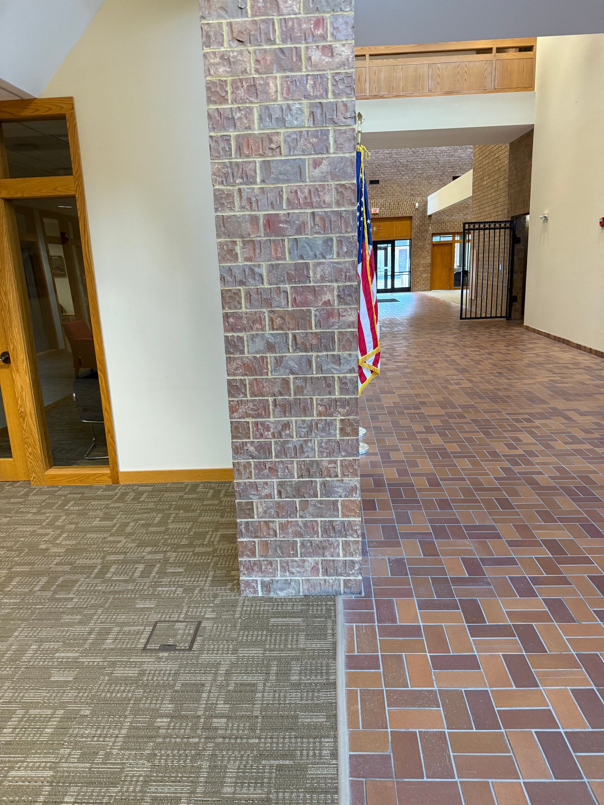 Hallway with brick floor, stone pillar, wooden doors, and an American flag on the right.