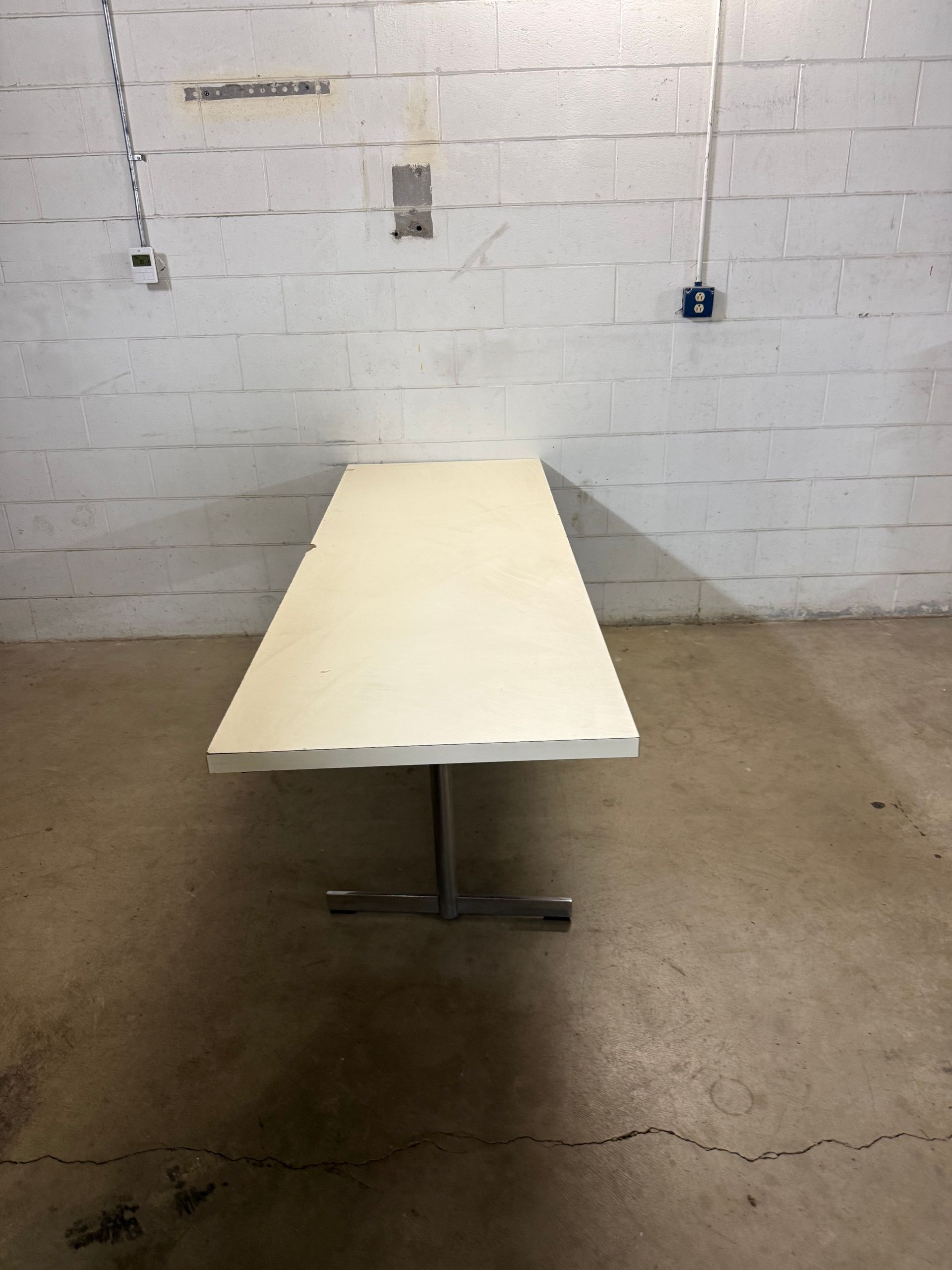 Long white folding table centered in a bare room with cinderblock walls and concrete floor