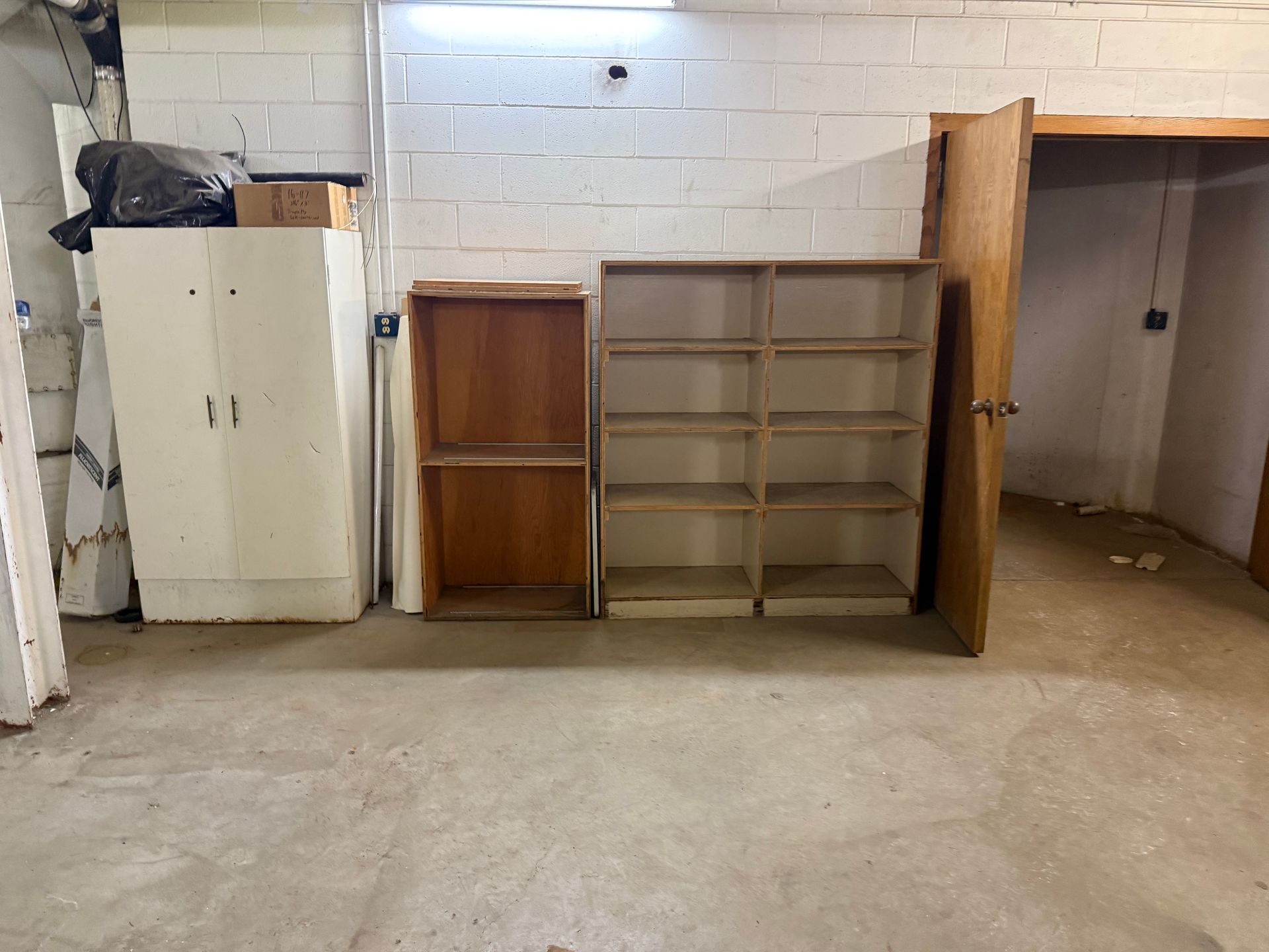 Storage area with shelves, cabinets, and a workbench against a white cinderblock wall.