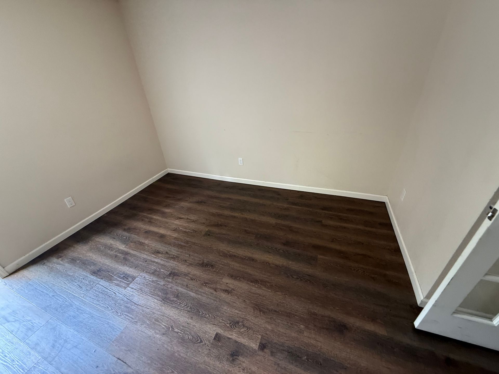Empty beige room with dark wood flooring and an open door on the right