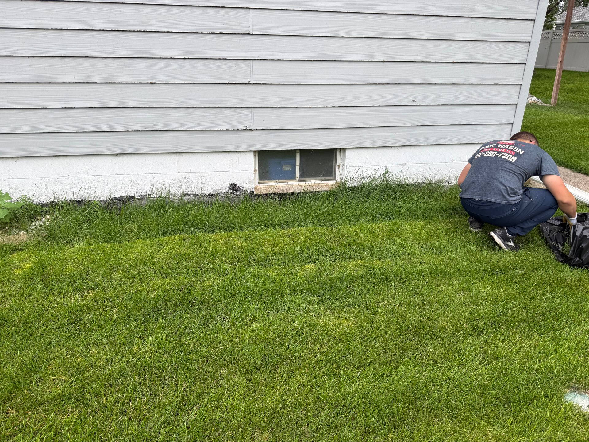 Piled wooden boards and a broken cardboard structure beside a garage on a lawn