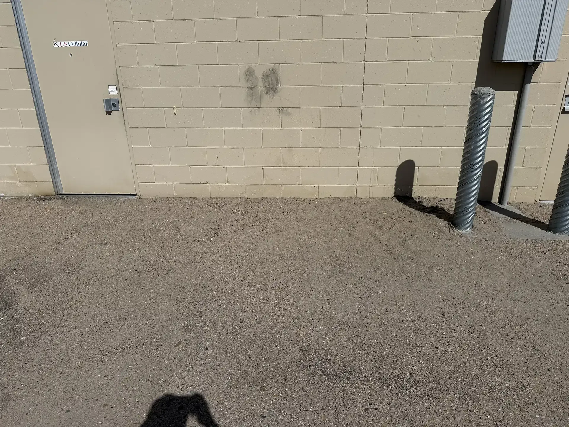 Exterior brick wall with a door, vent pipe, and gravel ground in sunlight
