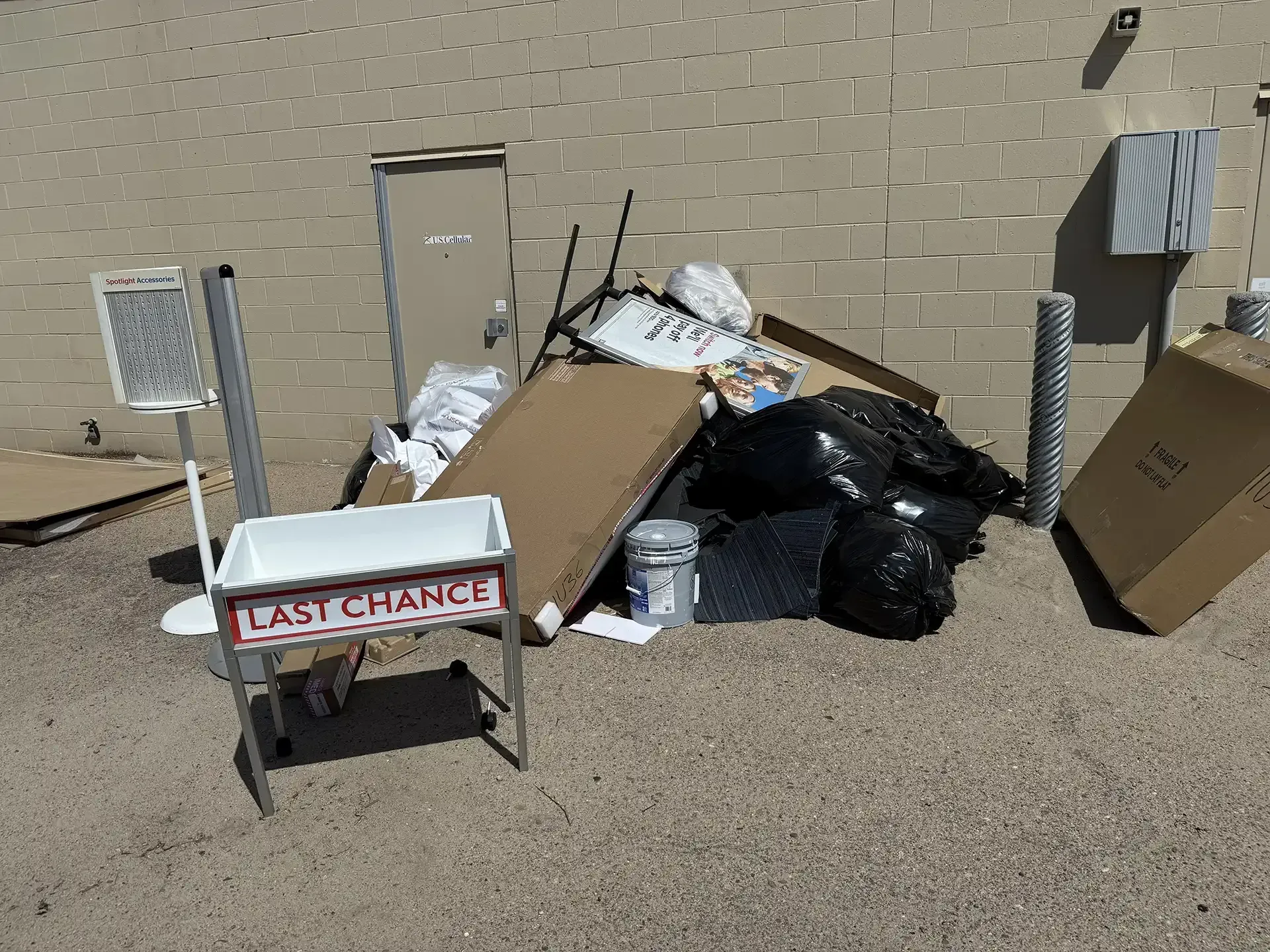 Overflowing trash and debris piled beside a tan brick wall, with a cart labeled “LAST CHANCE” in front.