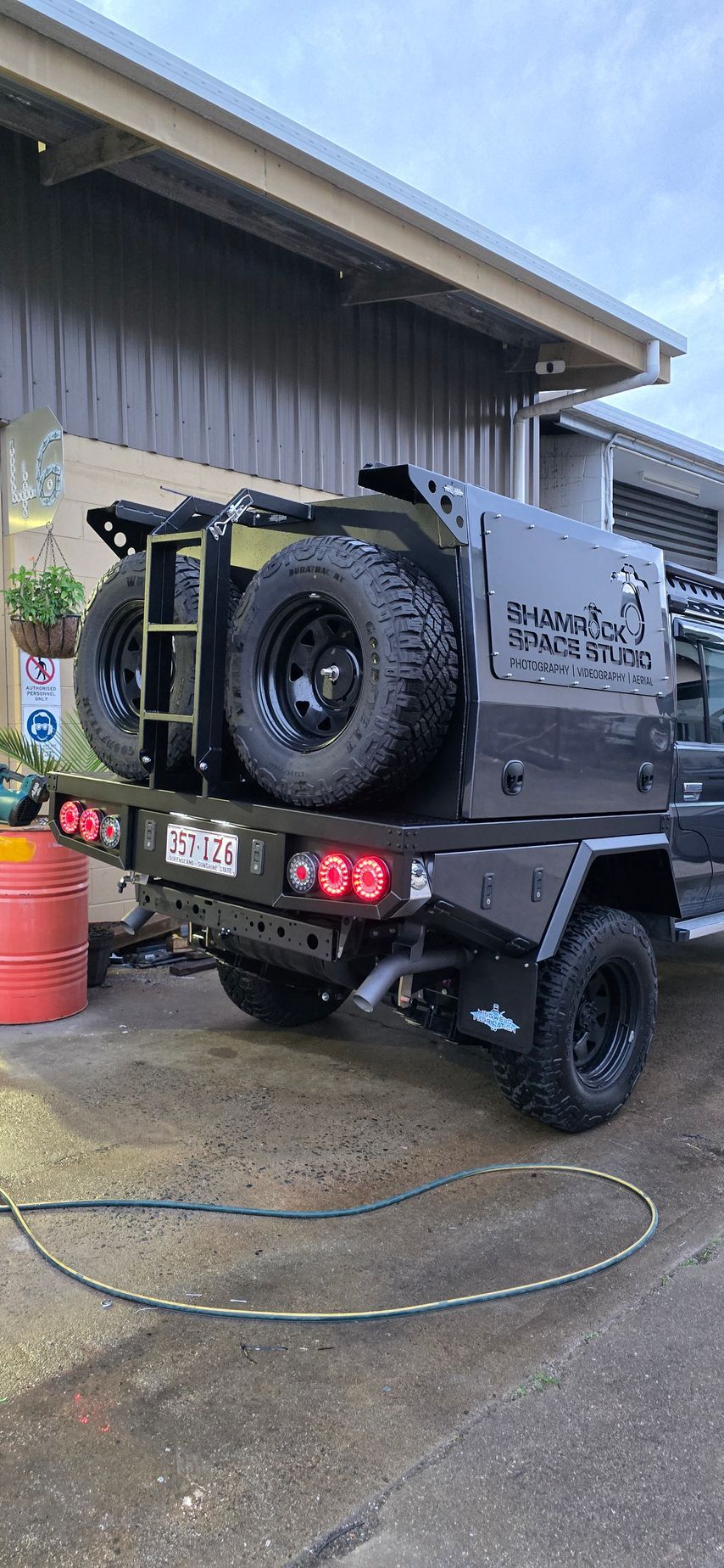 A black truck with large tires parked in front of a building. Two spare tires are mounted on the back — Mingweld Fabrication in Bungalow, QLD 