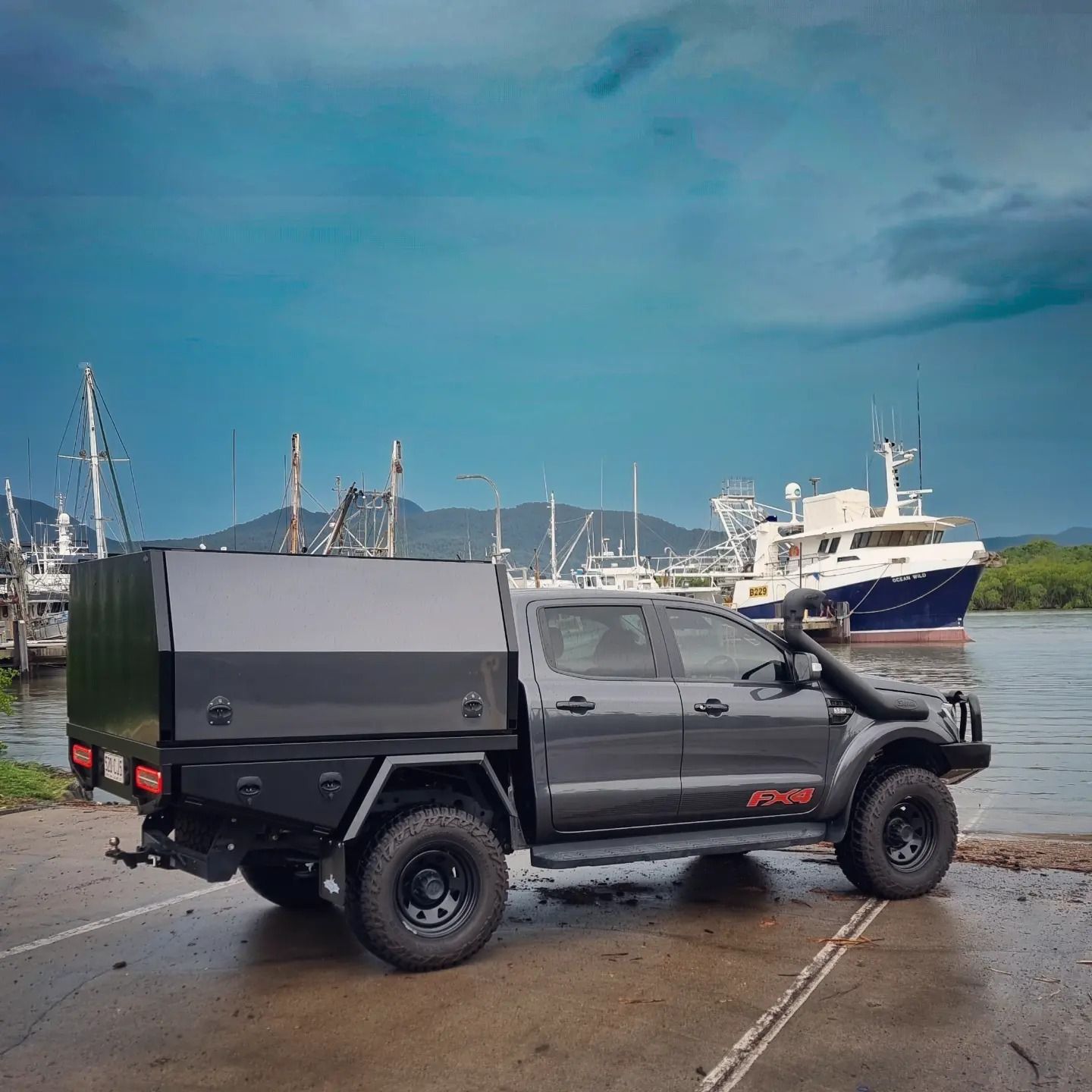 Dark grey pickup truck with black canopy, near water with boats and mountains — Mingweld Fabrication in Bungalow, QLD