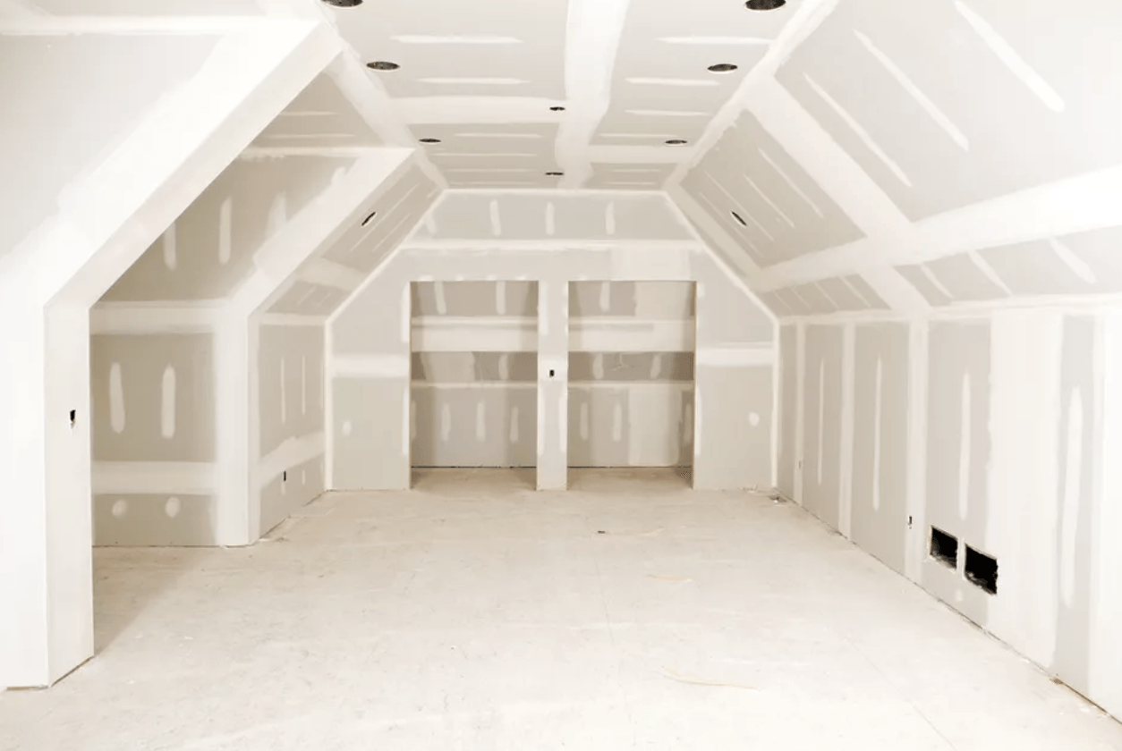 Empty unfinished room with white drywall, exposed beams, and bare concrete floor