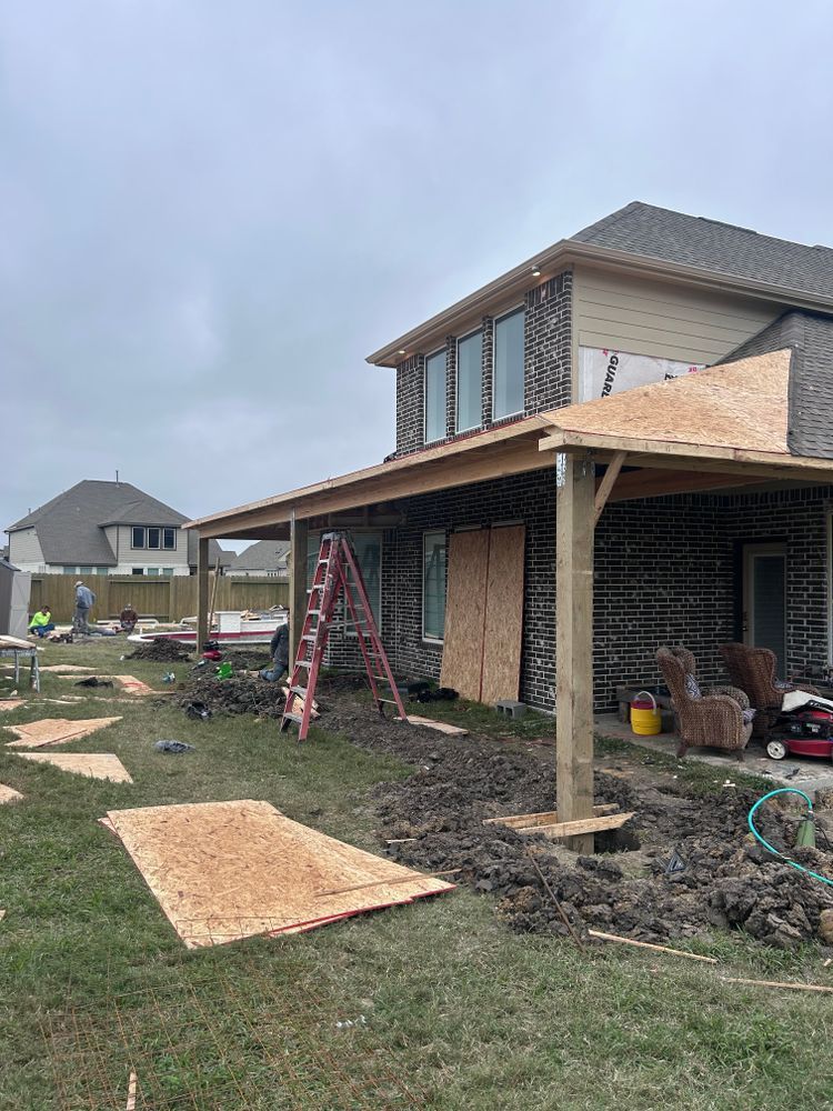 Construction of a covered patio on a brick house; framing, plywood, and lumber visible.