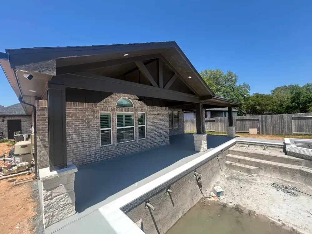 Covered patio with dark brown beams and a brick wall overlooking a swimming pool under construction.