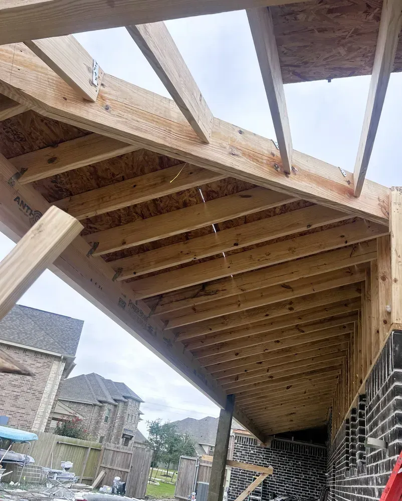 Wooden frame of a covered patio being built, attached to a brick house.