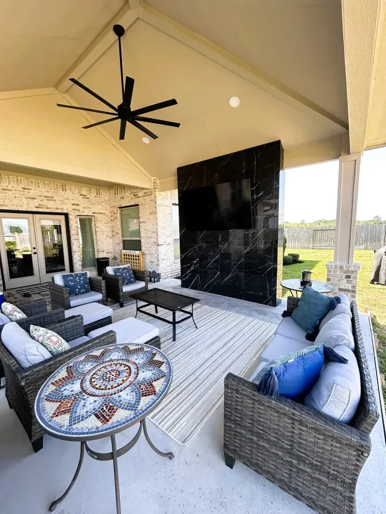 Covered outdoor patio with seating, TV, rug, and mosaic table. Features brick and a black accent wall.