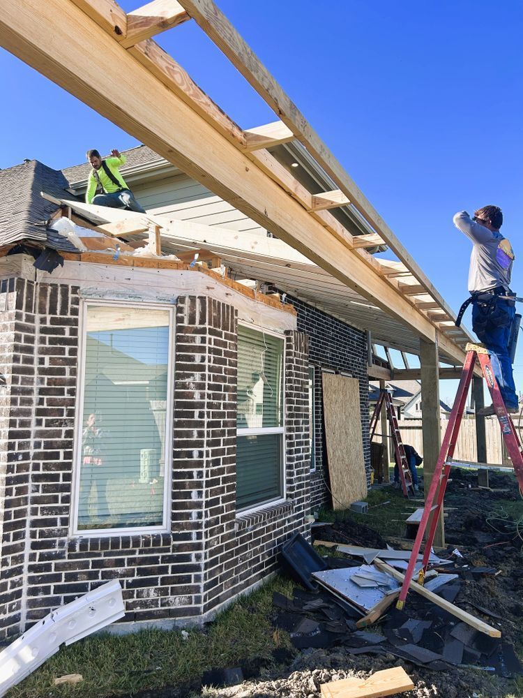 Construction workers building a porch roof on a brick house under a clear blue sky.