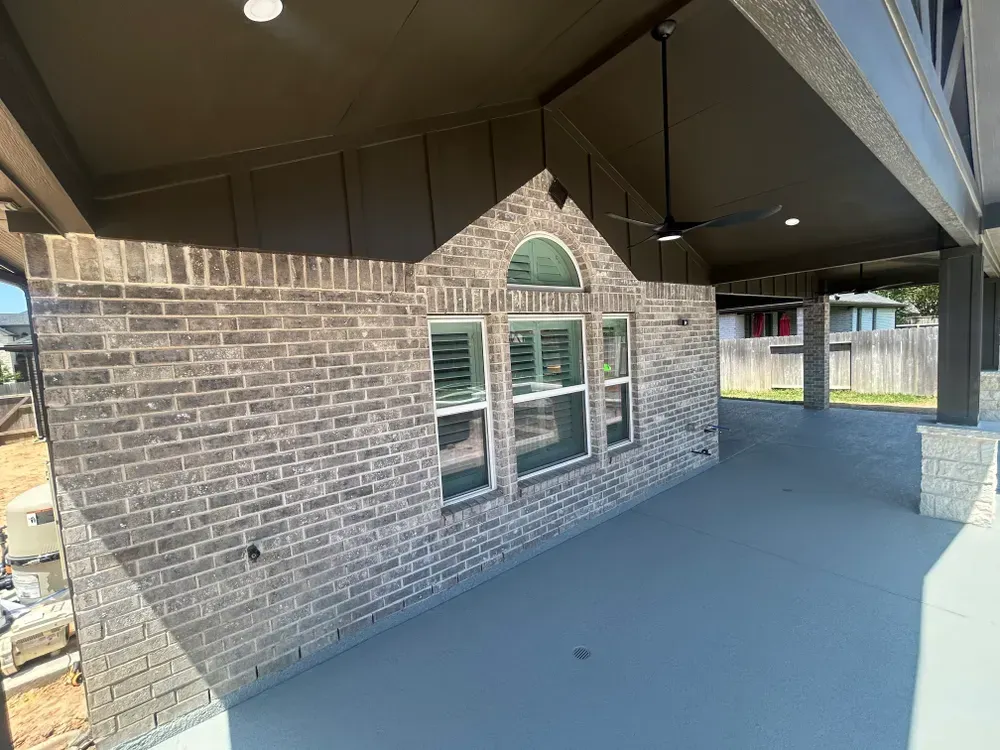 Covered patio with gray brick wall, windows, and a black ceiling fan.
