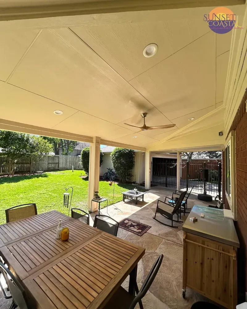 Covered patio with table, chairs, and grill; backyard with green lawn.