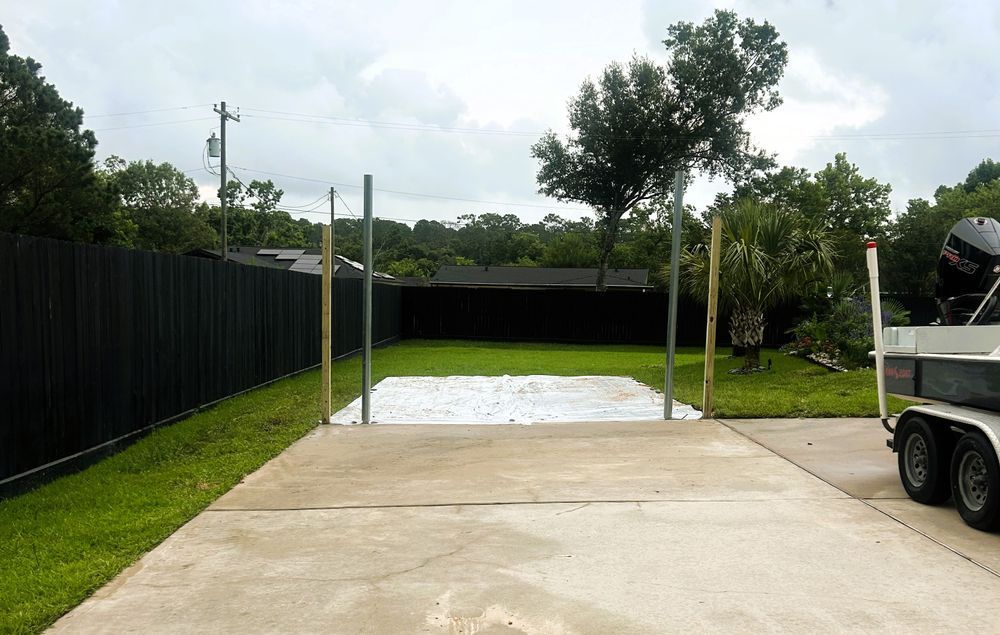Concrete slab with vertical poles, a boat trailer, and a dark fence in a yard.