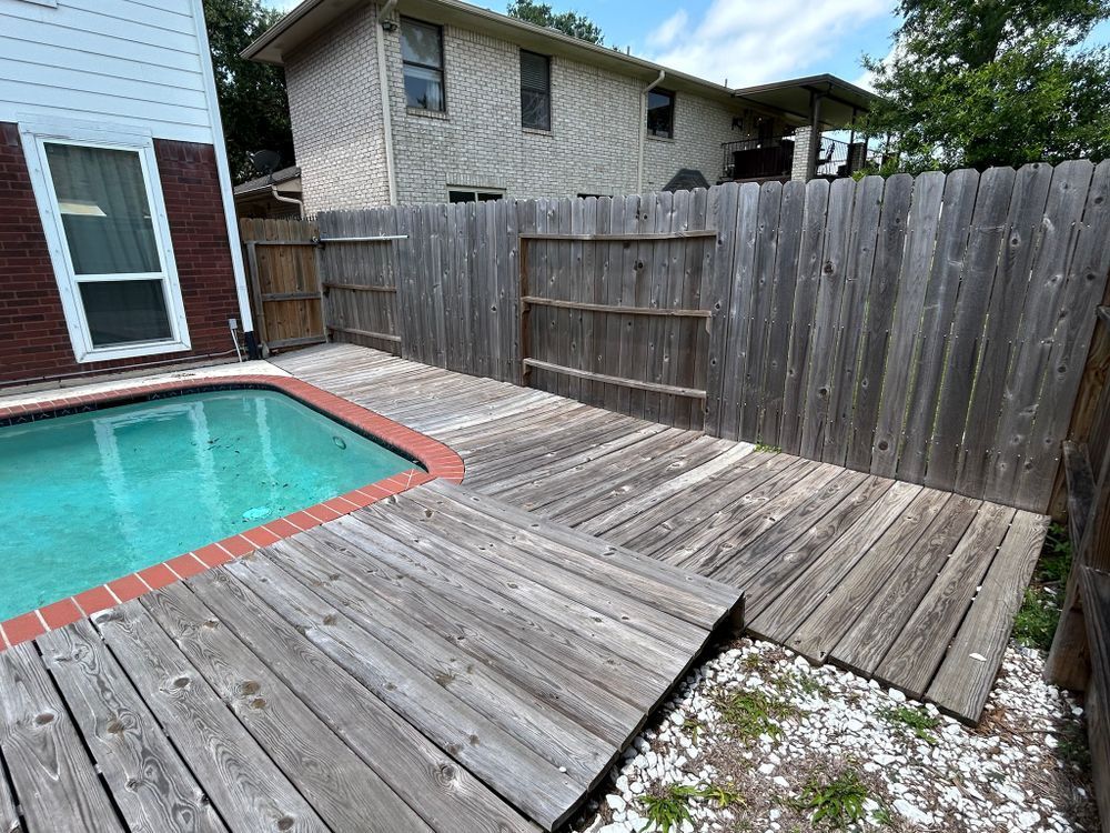 Wooden deck with weathered boards beside a pool, enclosed by a wooden fence.