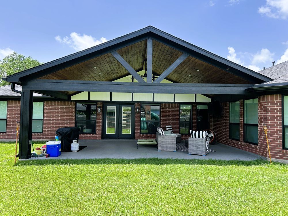 Black patio cover with a wooden ceiling, brick house, and patio furniture.
