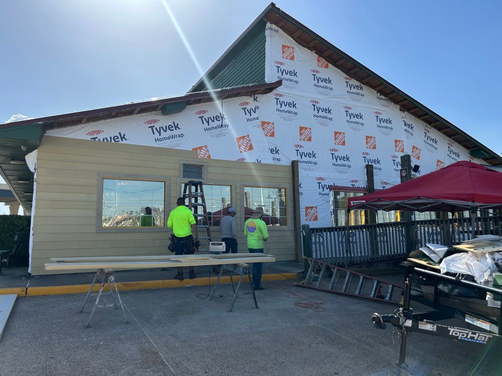 Construction workers siding a building, covered in Tyvek, under a bright sun.