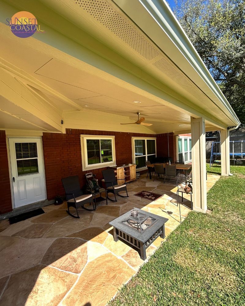 Covered patio with flagstone, brick wall, furniture, and a fire pit in a backyard.