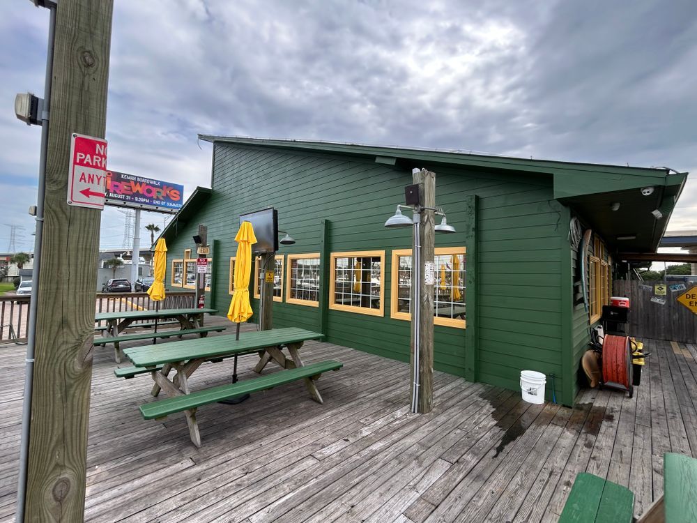 Green restaurant with outdoor seating and yellow umbrellas on a wooden deck under a cloudy sky.