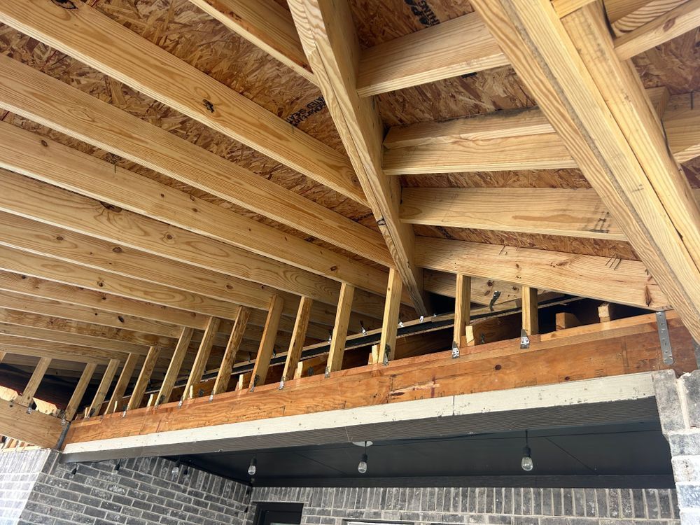Wooden roof trusses under construction above a brick wall and interior ceiling.