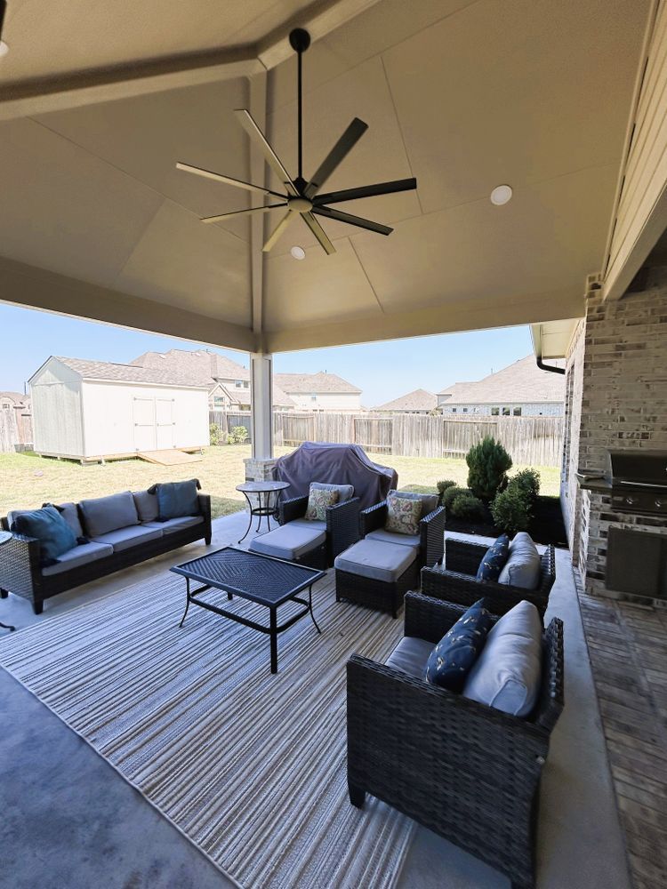 Covered patio with gray seating, black fan, and outdoor fireplace.