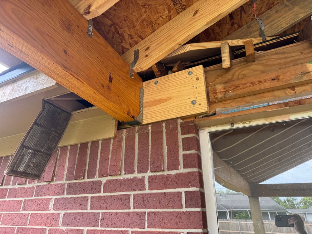 Wooden beam construction attached to a brick wall. Supporting structure of a roof or awning, with exposed wood and metal.