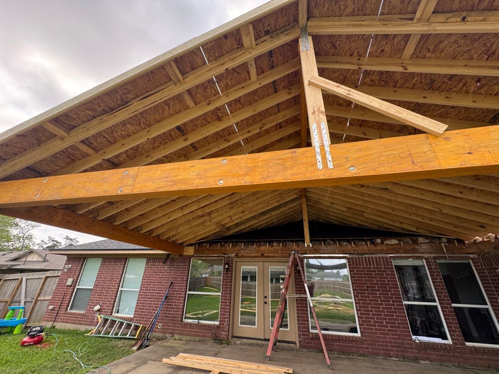 Construction of a covered patio on a red brick house; wooden frame with exposed rafters.