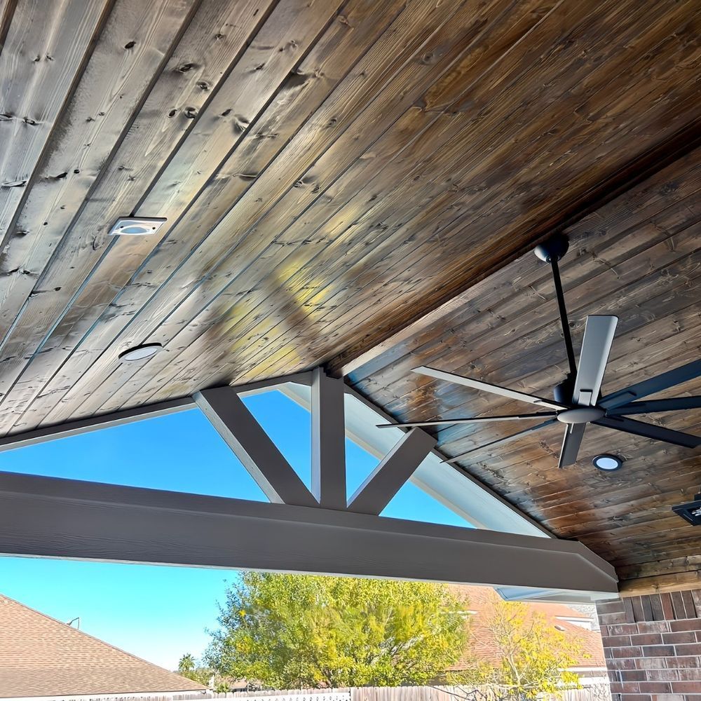 Wooden patio ceiling with a fan, beams, and recessed lights. Bright blue sky visible.