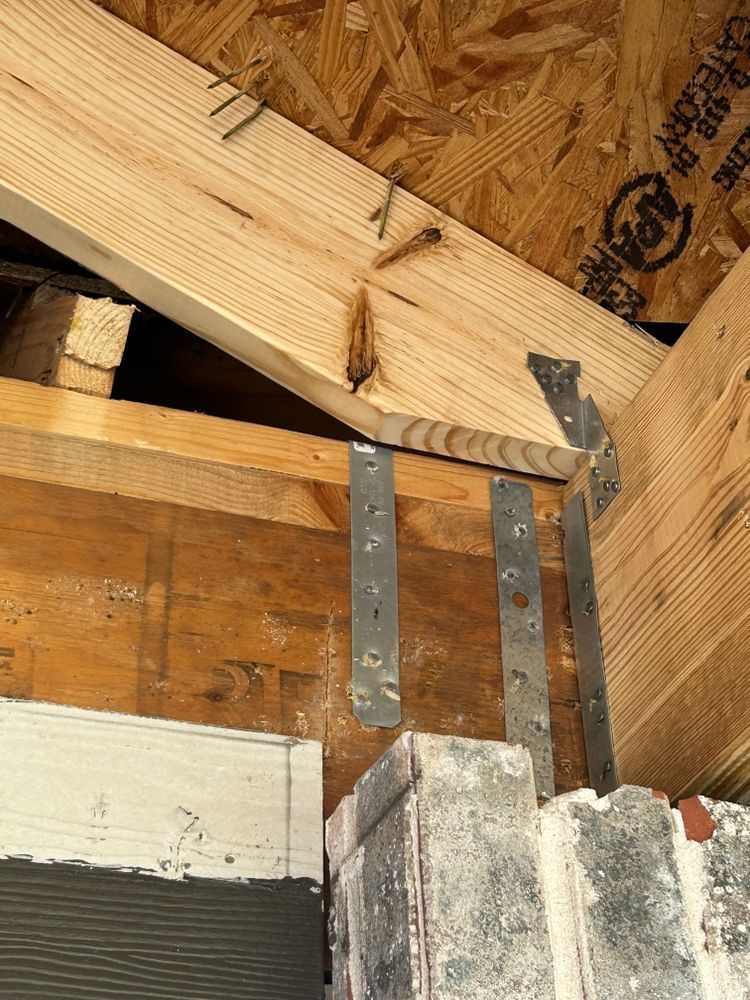 Wooden beams and metal straps securing roof structure to brick wall.