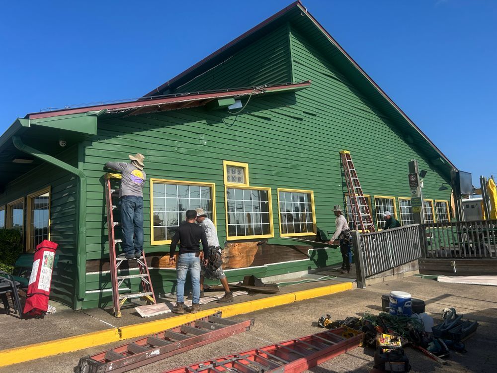 Construction workers on ladders repairing a green building with yellow trim.