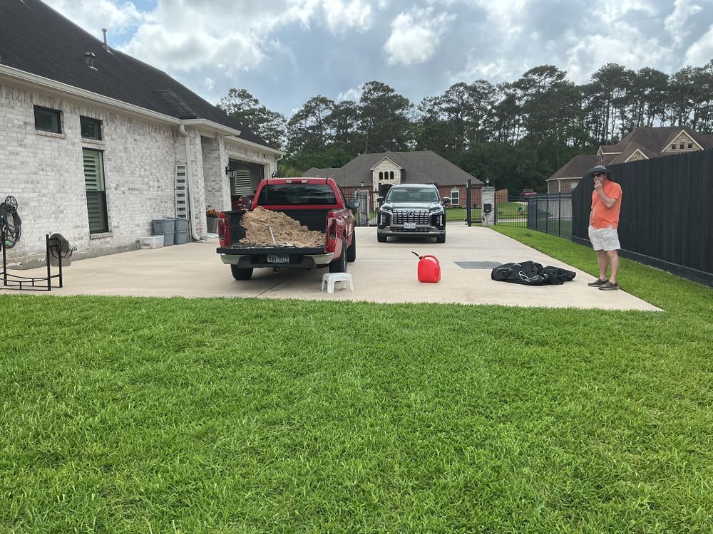 A backyard scene with a red pickup truck loaded with wood, SUV, and person standing near a black fence.