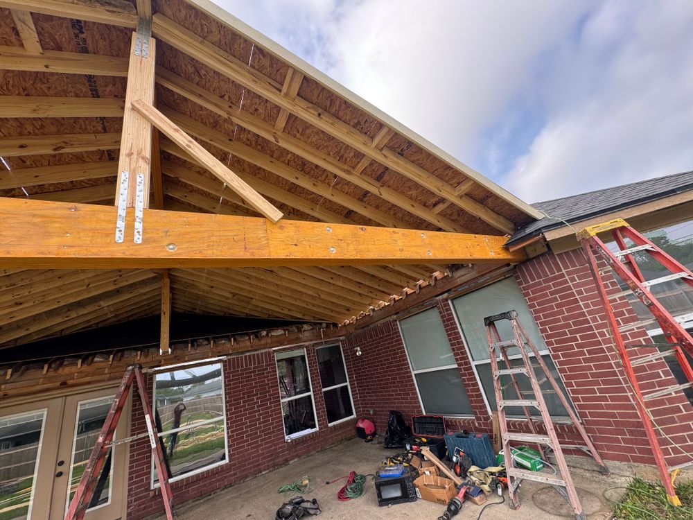 Construction of a wooden patio cover attached to a brick house. Ladders and tools present.