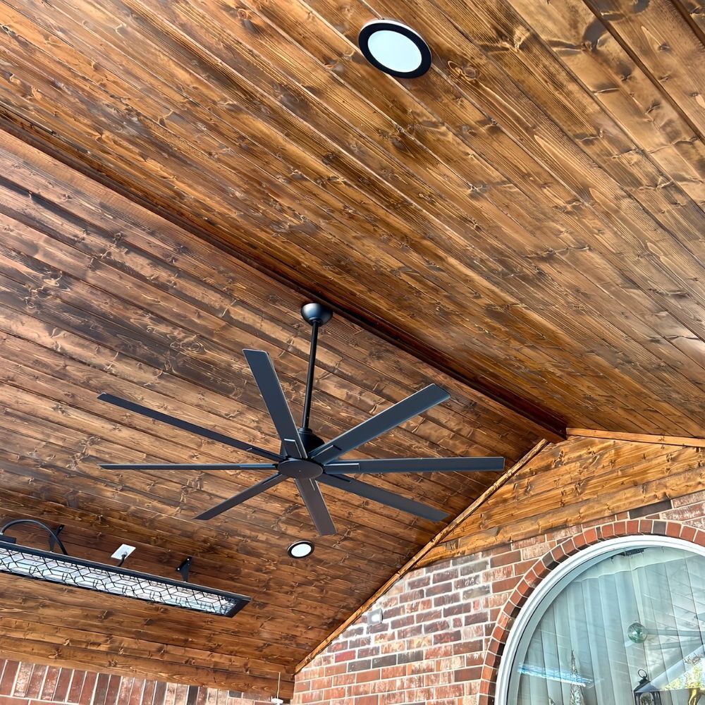 Wooden ceiling with recessed lights, a black ceiling fan, and a brick and window exterior.