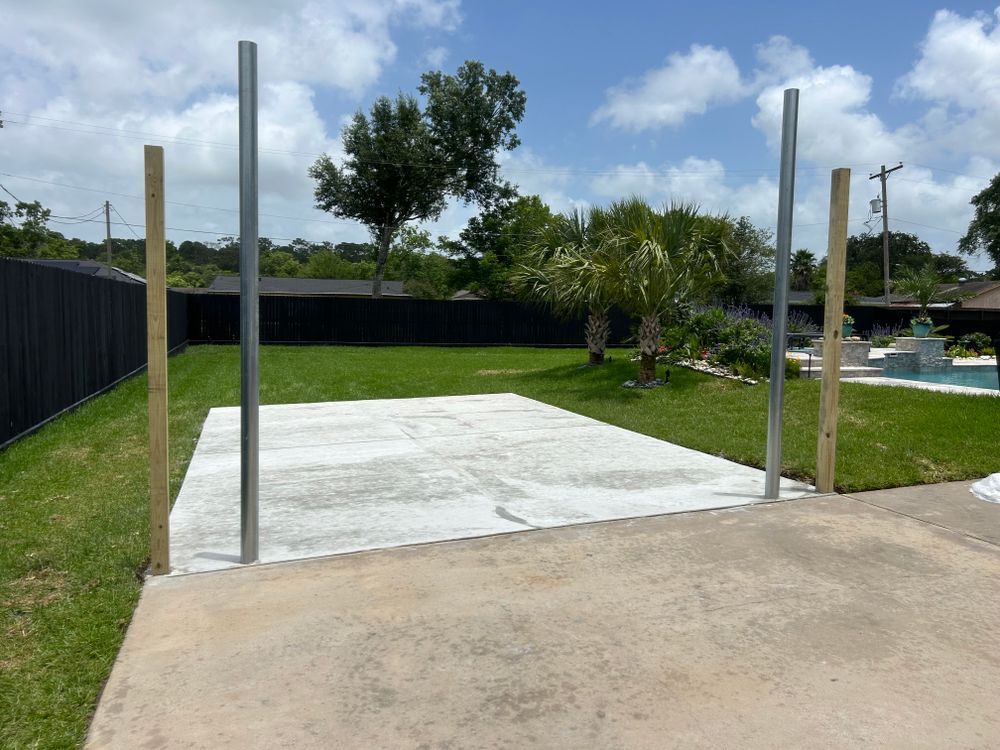 Concrete pad with four vertical posts in a backyard, ready for construction.