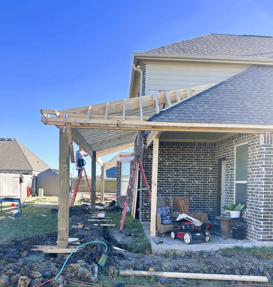 Construction of a wooden patio cover attached to a brick house. Workers, ladders, and tools are visible.