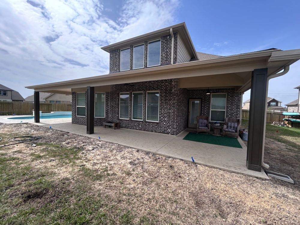 A two-story brick house with a covered patio overlooking a pool on a sunny day.