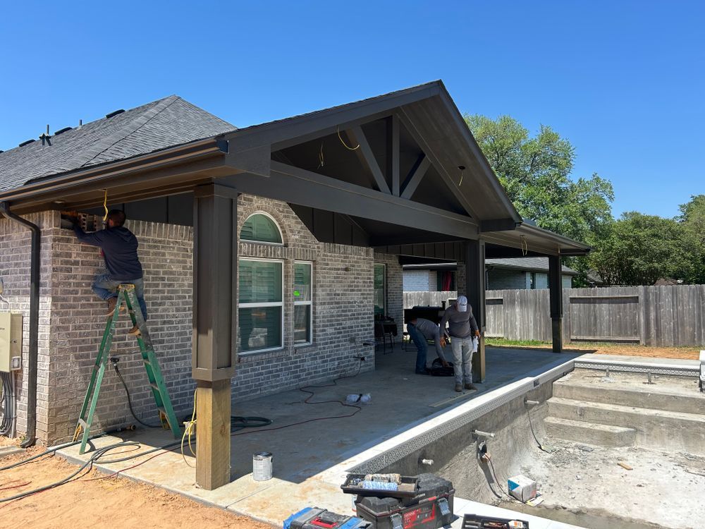 Construction workers installing a wooden patio cover on a brick house next to a pool.