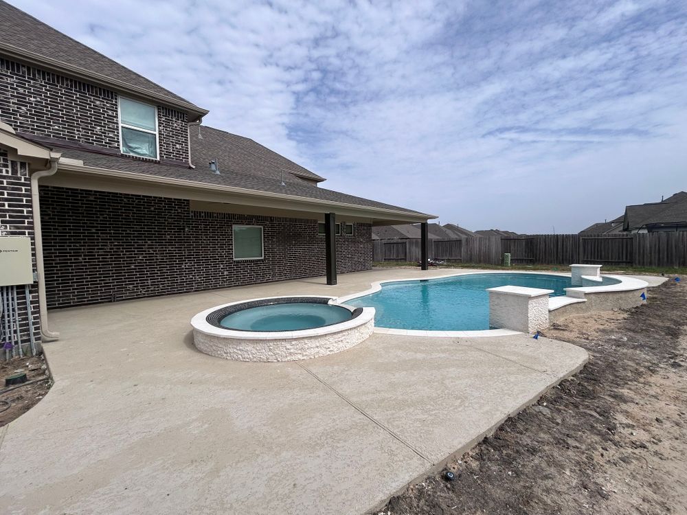 Pool with spa, patio under house awning. Blue water, light concrete, brick house.