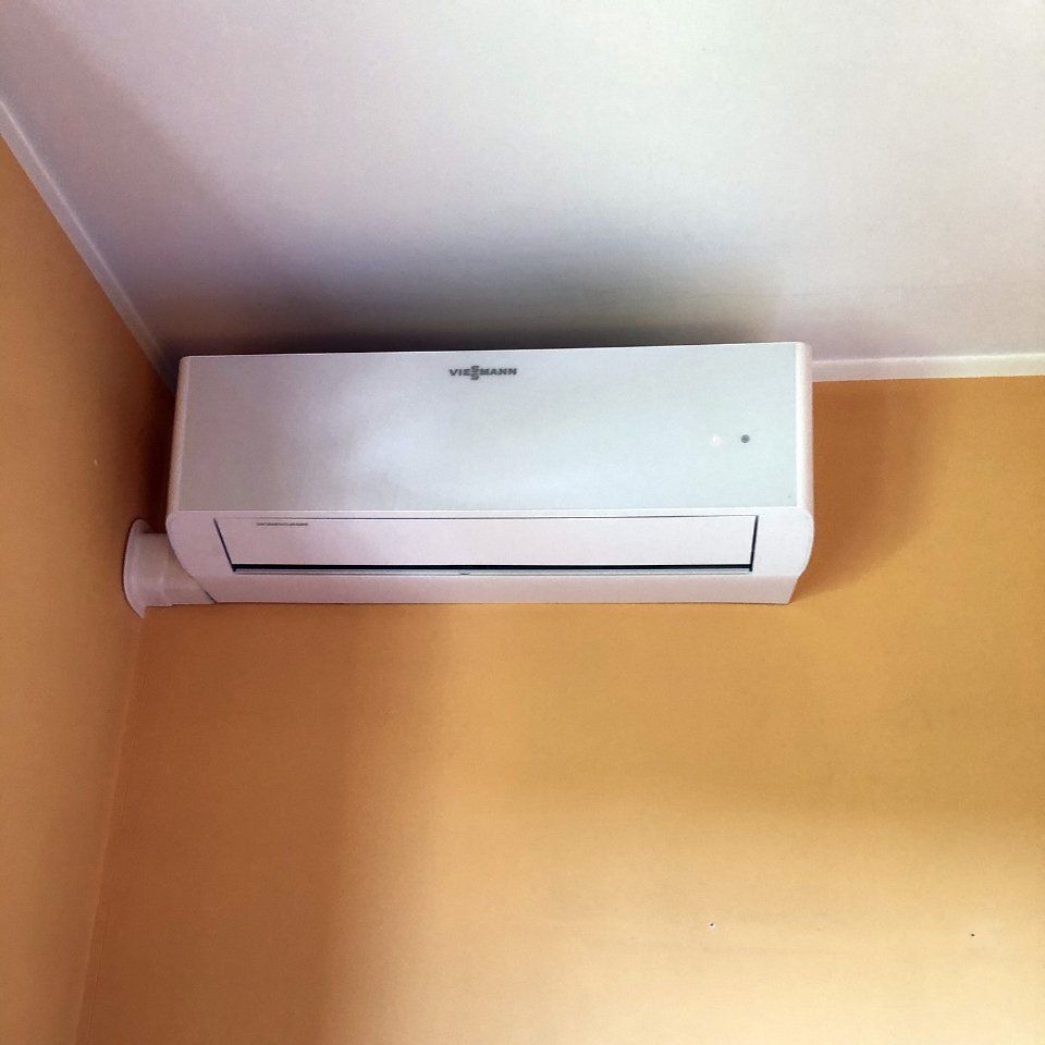 Condizionatore d'aria bianco montato su una parete marrone chiaro, sotto un soffitto bianco.
