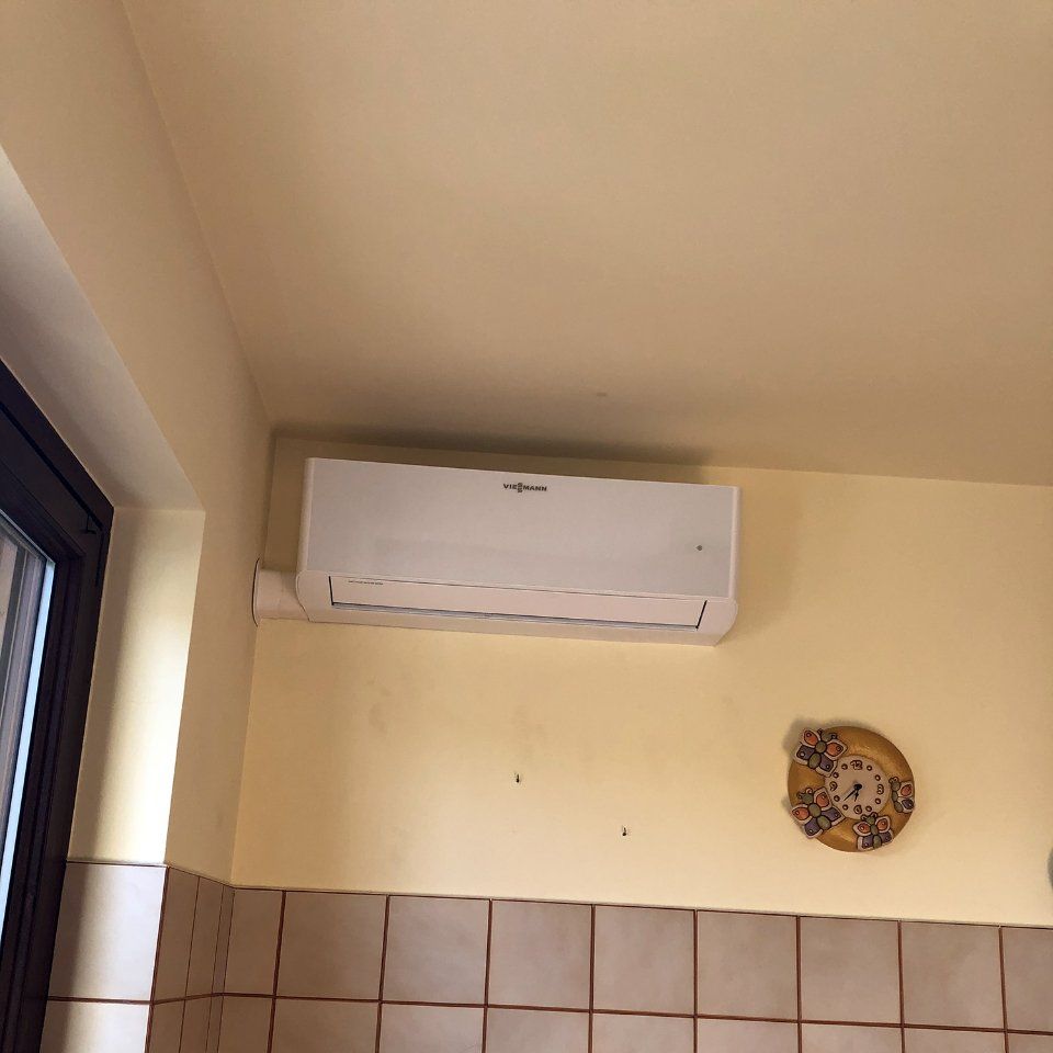 Condizionatore d'aria montato su una parete gialla con piastrelle beige sottostanti. Sulla parete è presente anche un piatto decorativo.