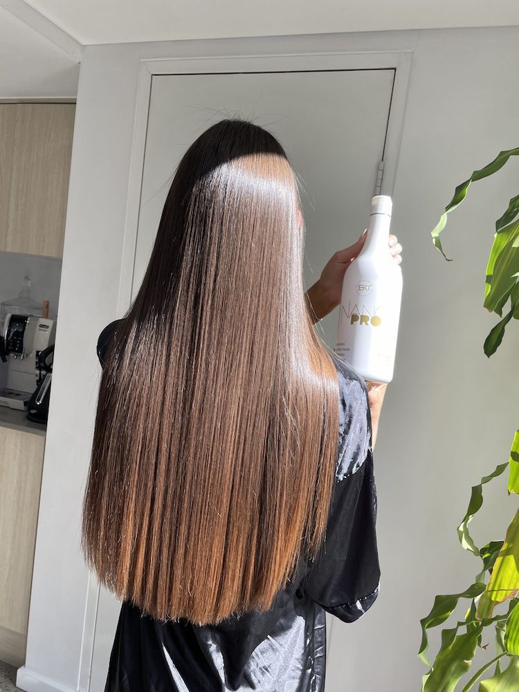 A Woman With Long Hair is Holding a Bottle of Shampoo — Tree House Salon In Nerang, QLD