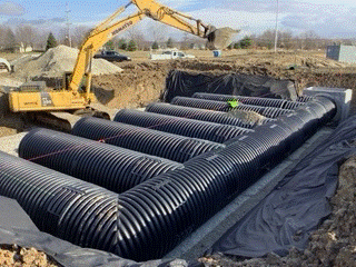 A yellow excavator is working on a large drainage system.